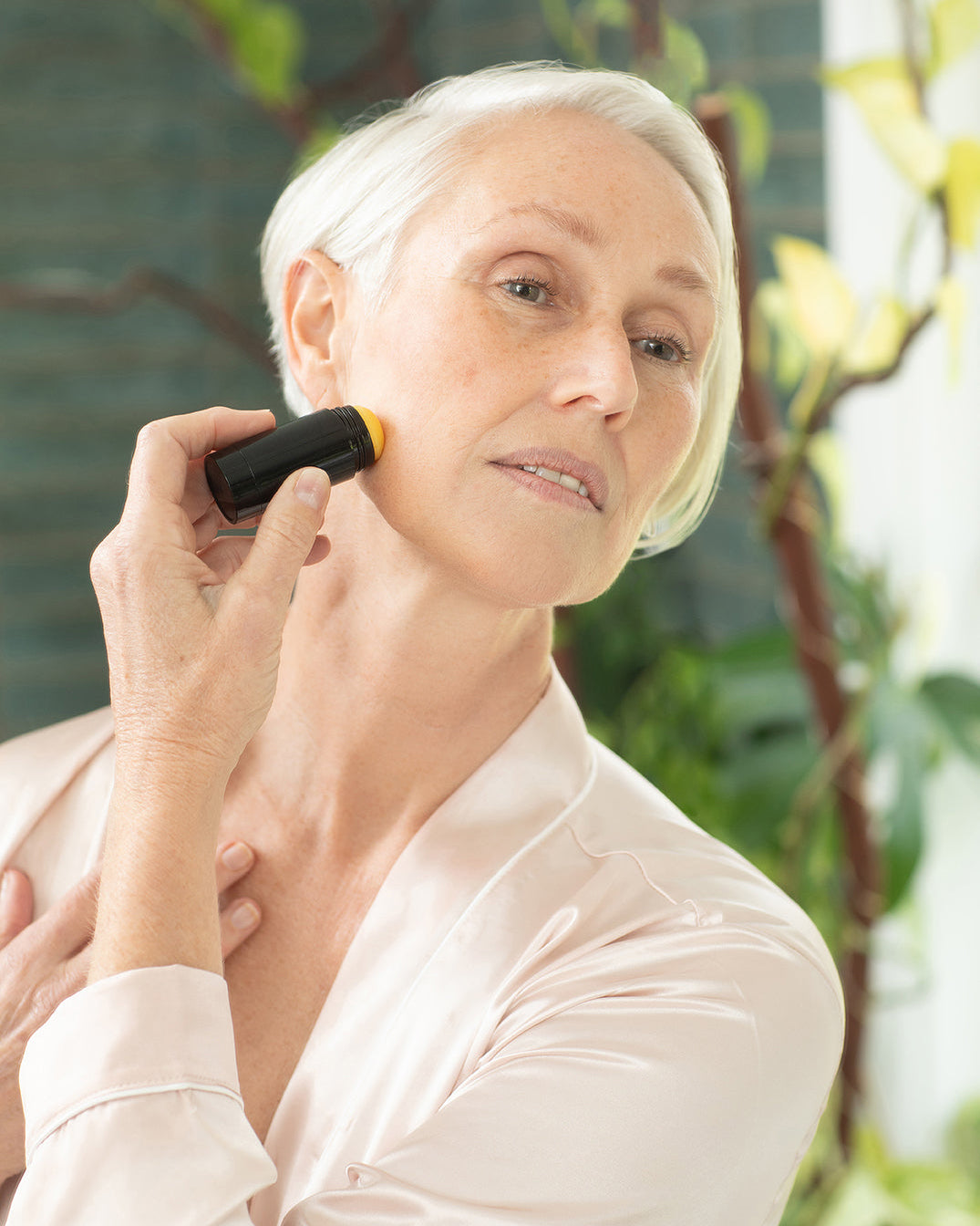Barbi gliding the PHILOGENI Resilience Balm stick across her cheekbone in soft morning light.