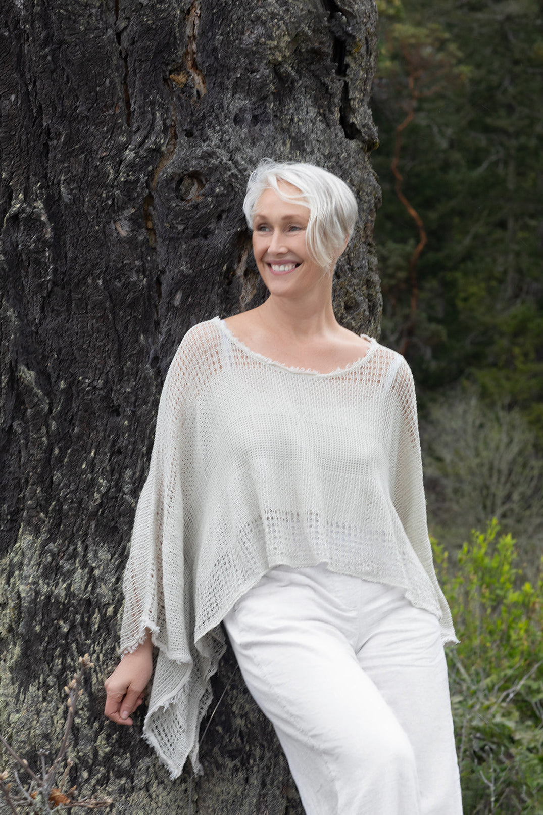 A woman in white linen resting against a moss-covered trunk